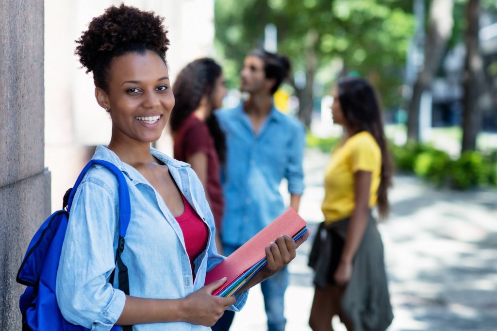 Laughing african american female student in front of university outdoor in summer in city